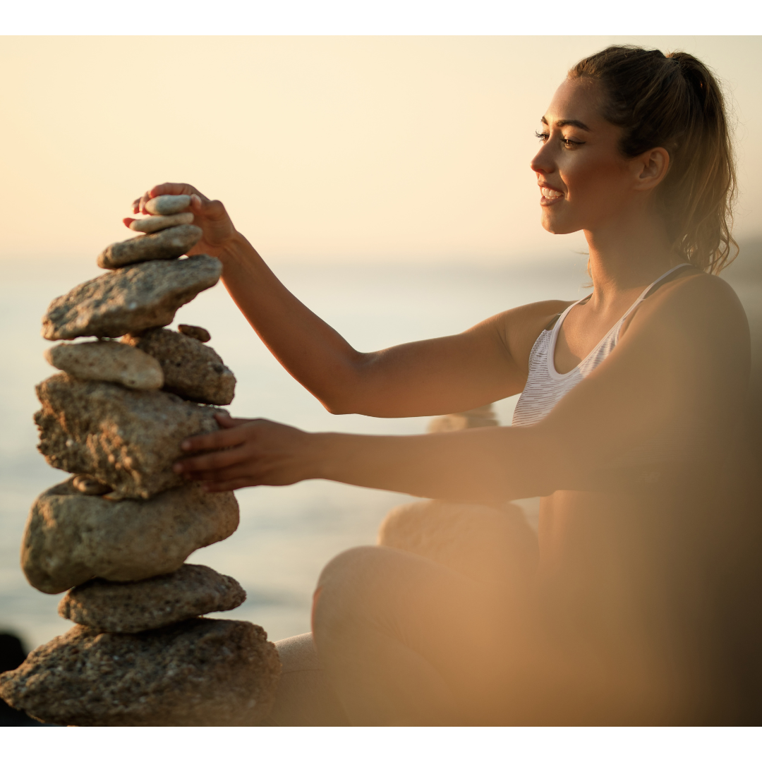 Frau am Meer stapelt Steine bei Sonnenuntergang, Symbol für innere Balance durch Lithium Orotat von Doktor Health.